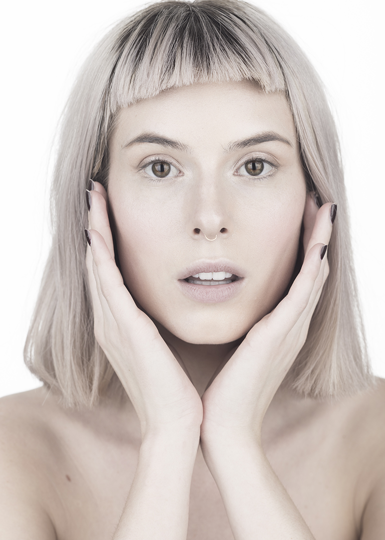 A portrait of a woman with fair skin holding the sides of her face.