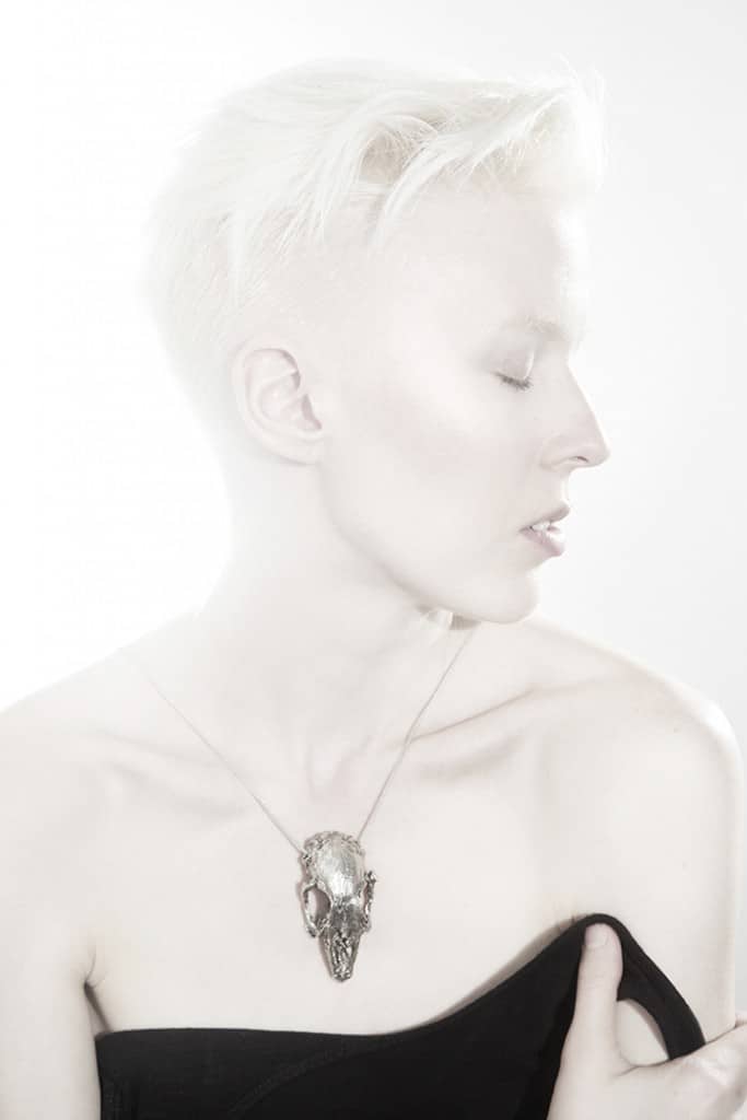 A studio portrait of a woman with fair skin wearing a silver necklace and black tube top.