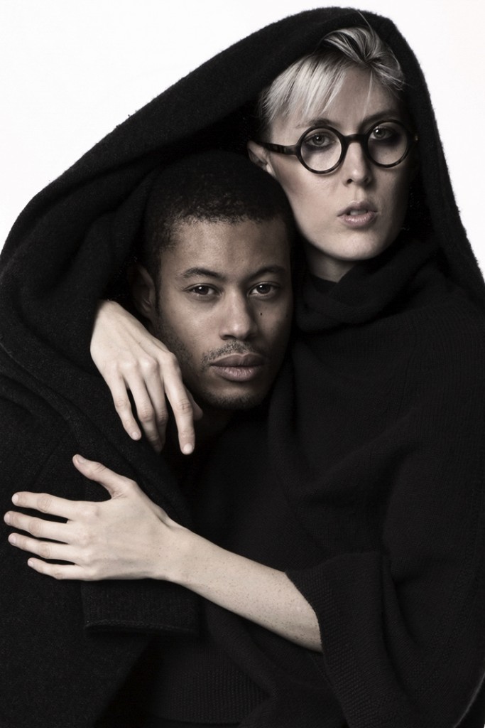 A studio portrait of a black and white couple with a black garment wrapped around them.