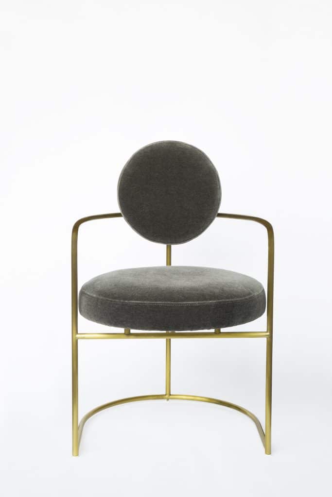 A studio product shot of a grey chair with gold hardware on a white background.